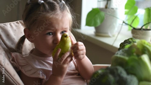 Young baby girl eats fresh pear. Healthy food. Vitamins and healthy raw fruct from an early age for babies. Proper nutrition photo
