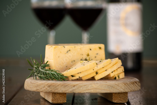 Queso manchego con epazote sobre una tabla de madera y copas de vino al fondo delicioso aperitivo photo