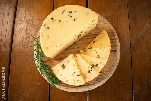 Toma zenital de un queso manchego entero y en rodajas sobre una tabla de madera con epazote  photo