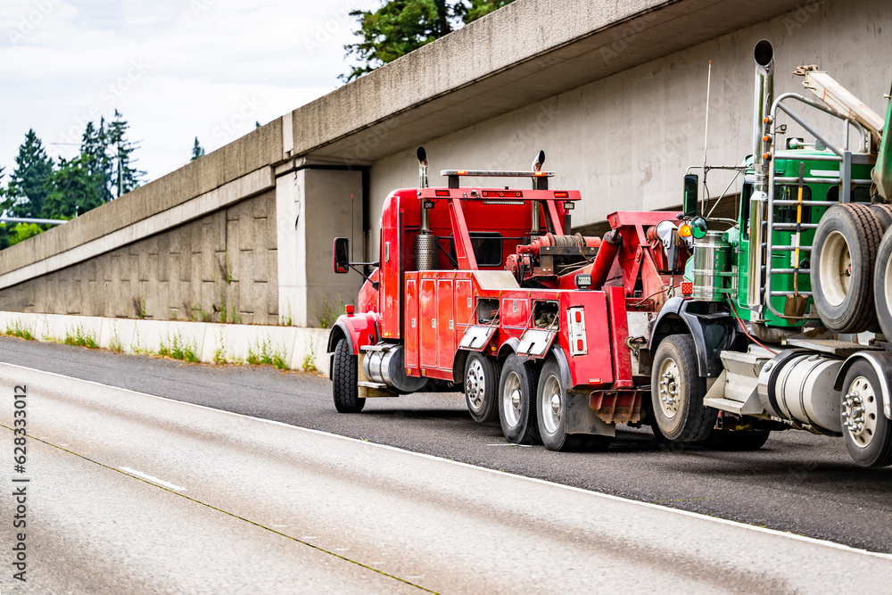 Obraz premium Mobile road assistant red big rig tow semi truck towing broken green semi truck picking up it on the highway road shoulder