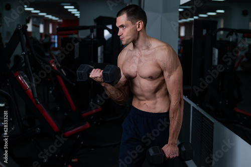 Shirtless man doing bicep exercises with dumbbells in the gym. 