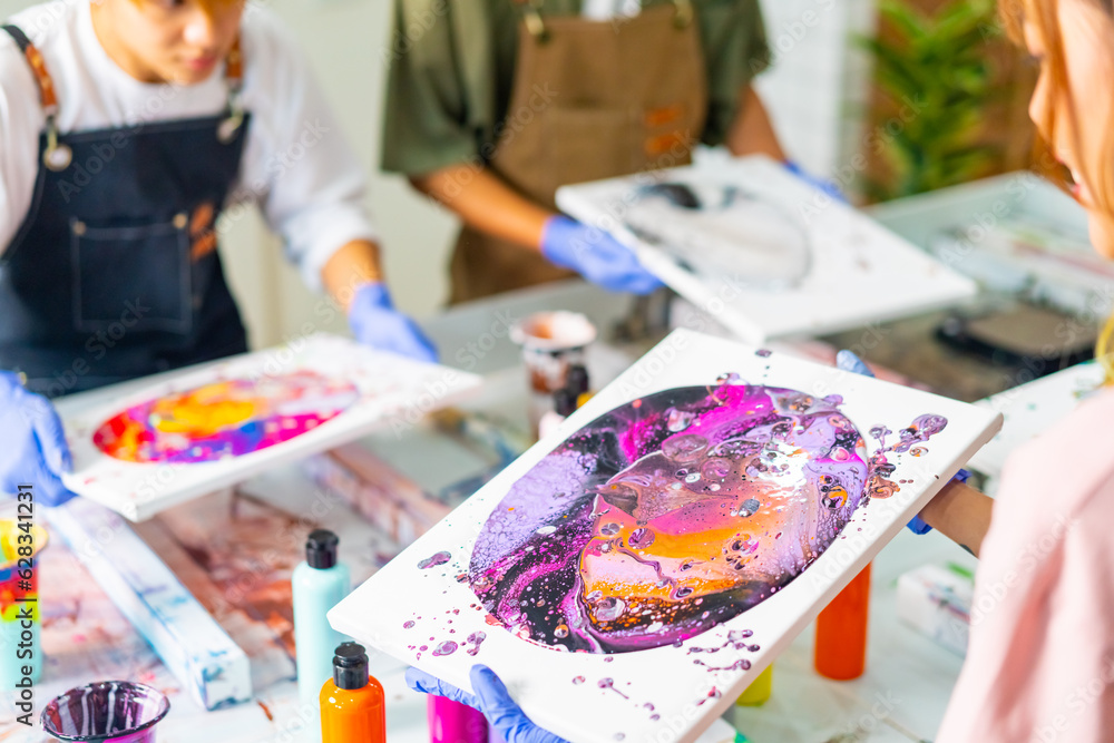 Group of Asian generation z people learning acrylic pouring art on canvas workshop at art studio. Young artist university student enjoy and fun creating colorful abstract modern art painting in class. Group of Asian generation z people learning acrylic pouring art on canvas workshop at art studio. Young artist university student enjoy and fun creating colorful abstract modern art painting in class.