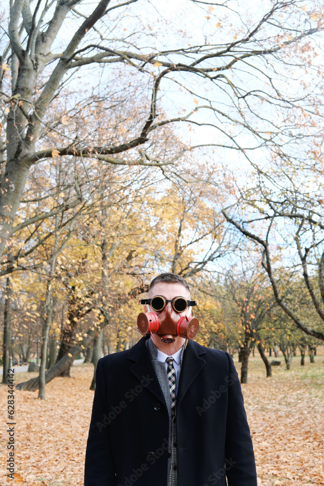 Businessman standing in autumn park wearing gas mask Businessman standing in autumn park wearing gas mask