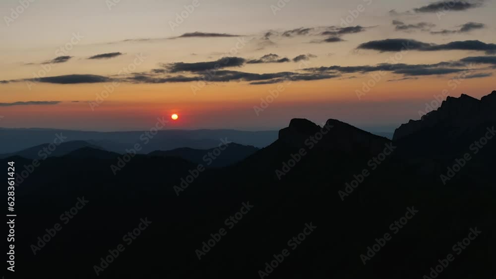 Beautiful mountain sunset. Time-lapse of sunset with clouds against silhouette of mountain peaks. Red sun hiding behind high mountains Beautiful mountain sunset. Time-lapse of sunset with clouds against silhouette of mountain peaks. Red sun hiding behind high mountains