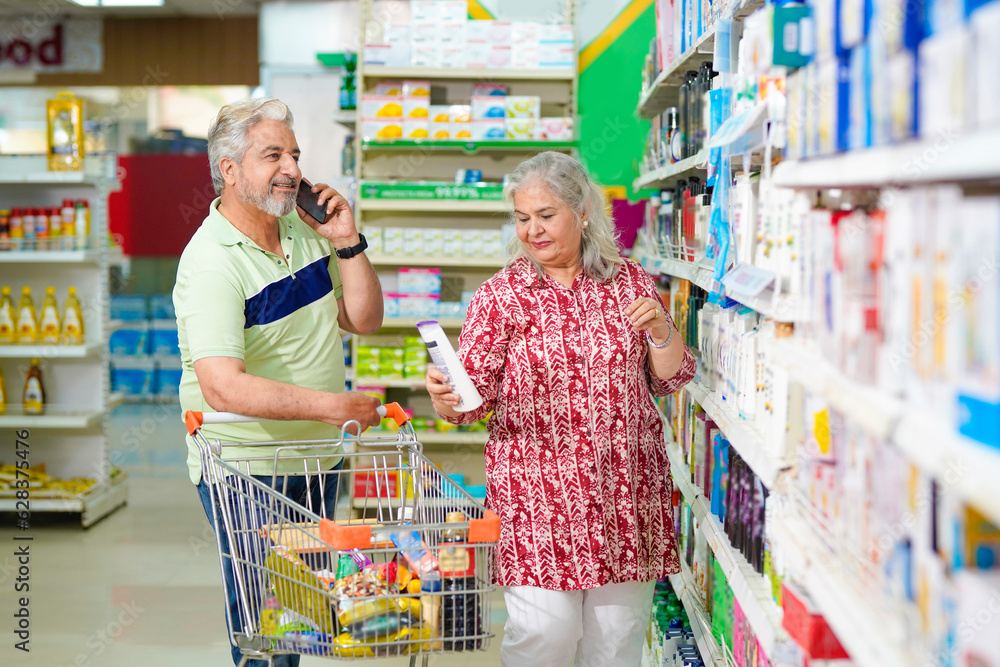 Senior man talking on smartphone and woman shopping at grocery shop.