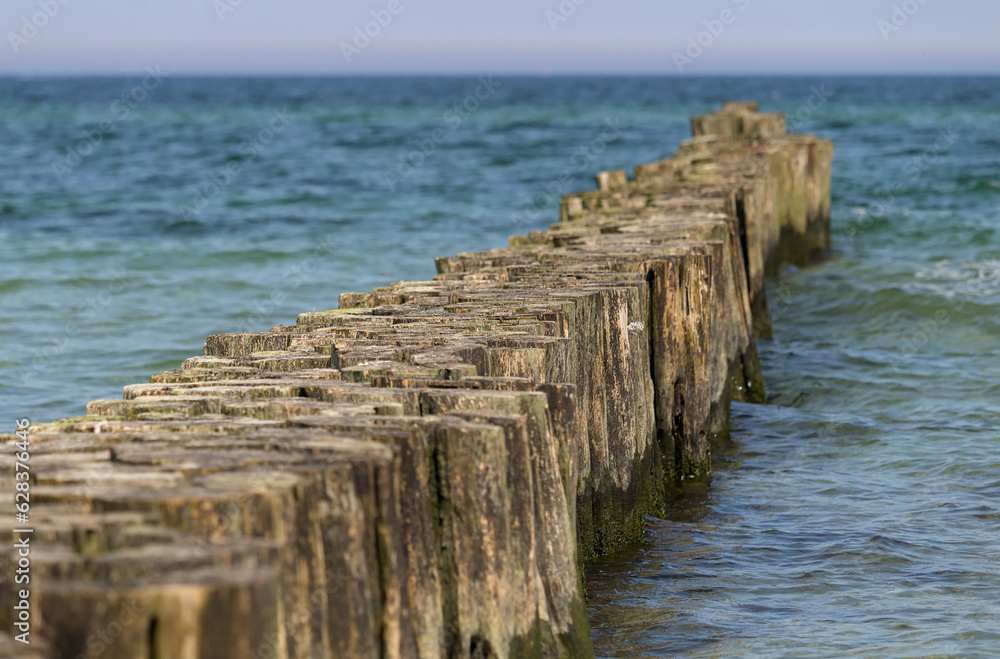Wooden breakwater in the blue turquoise Baltic Sea with horizon and calm water. Diagonal.