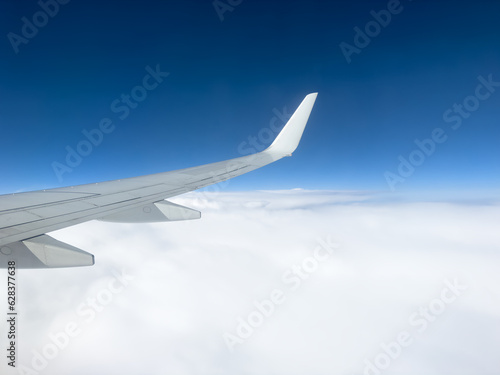 White wing from airplane window on sunny day. Great views of landscape. Aerial view of clouds through a plane window. Wing of airplane with blue sky and beauty clouds