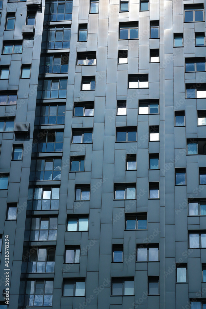 Facade with windows of a dark multi-apartment residential high-rise building. Vertical photo.