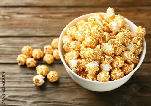 Bowl with tasty caramel popcorn on wooden table MADE OF AI