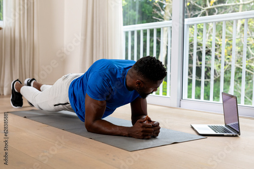 African american man exercising on mat using laptop at home