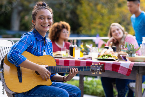Portrait of happy diverse group of friends playing guitar and having dinner