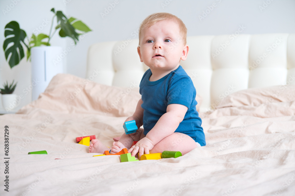 baby boy in blue bodysuit playing with colorful wooden eco toys on bed baby boy in blue bodysuit playing with colorful wooden eco toys on bed