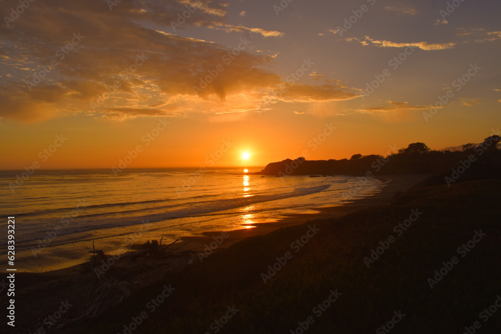 Stunning bright orange and gold sunset on fire over calm ocean with gentle waves ,lapping the shoreline Stunning bright orange and gold sunset on fire over calm ocean with gentle waves ,lapping the shoreline