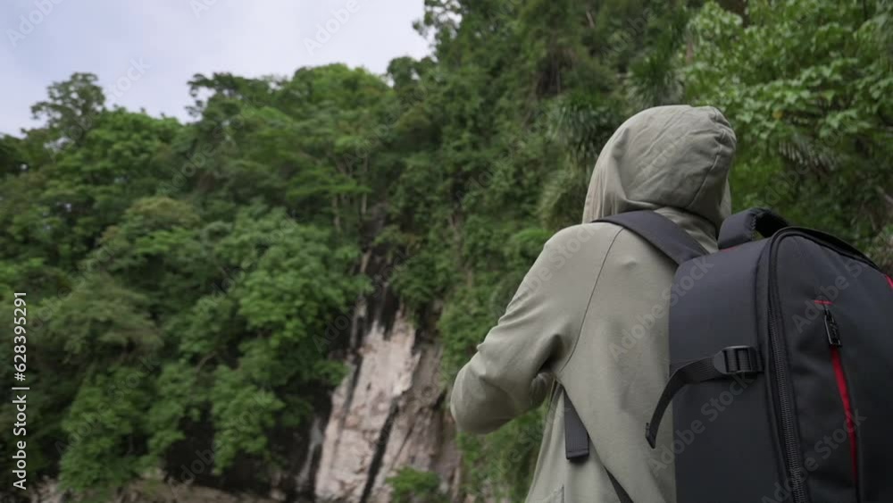 Rear view of female traveler recording video with digital camera panning shot beautiful scenery of lush foliage plants covering the steep cliff. Solo nature adventure. Outdoor pursuit. Hobbies. Rear view of female traveler recording video with digital camera panning shot beautiful scenery of lush foliage plants covering the steep cliff. Solo nature adventure. Outdoor pursuit. Hobbies.