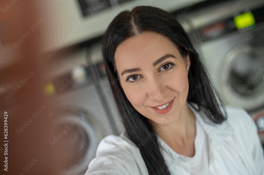 Woman waiting in a laundry room and making selfie on smartphone. Woman waiting in a laundry room and making selfie on smartphone.