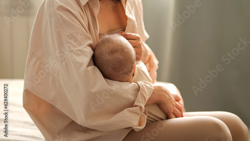 Mother breastfeeding baby daughter in spacious bedroom. Infant girl wanting to eat rests in exhausted parent arms in empty nursery