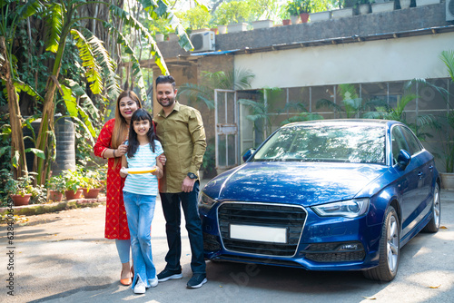 Indian family standing with new car. girl holding puja thali in hand.