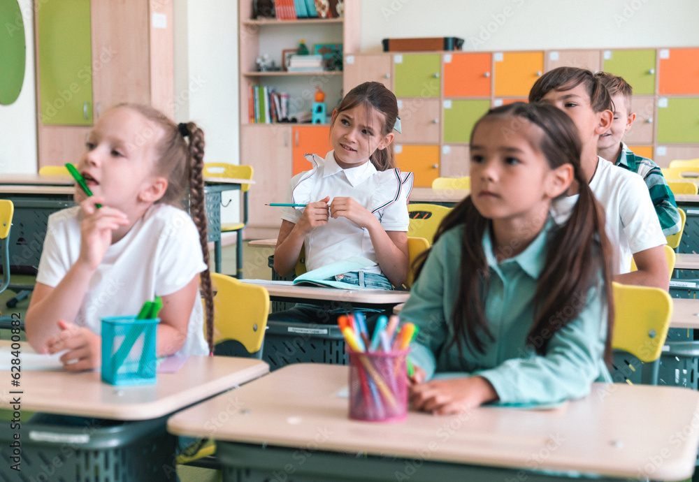 Elementary School and People Concept. Diverse excited group of emotional happy junior school kids sitting at desks in classroom Elementary School and People Concept. Diverse excited group of emotional happy junior school kids sitting at desks in classroom