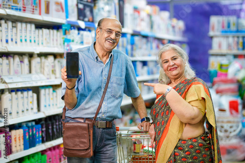 Senior man showing smartphone with his wife at grocery shop.