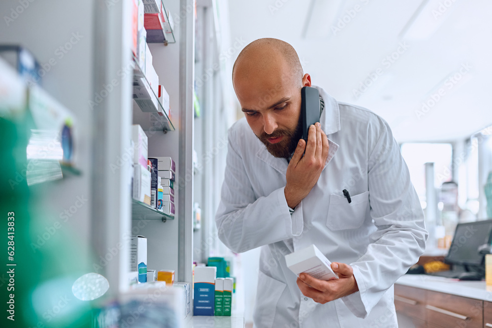 Male pharmacist talks on cell phone while looking for medicine in drugstore.