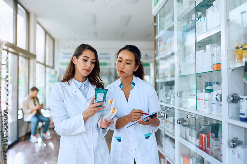 Young pharmacist and her female coworker going through merchandise inventory in drugstore.