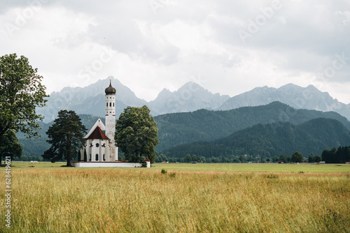 View of St. Coloman church near Schwangau on cloudy day, Alps in background photo