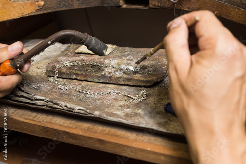 Close-up of the hands of a jeweler making repairs to a silver bracelet.