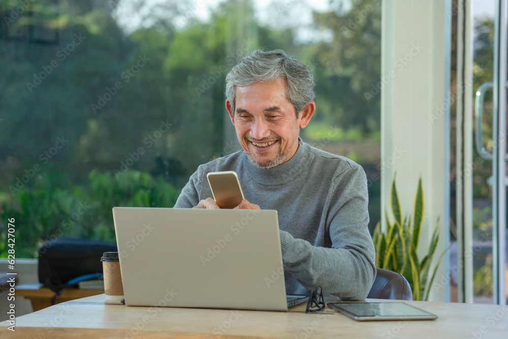 mature asian man working remotely on internet online over laptop and smartphone technology vacation,take a break in cafe at resort garden,destination in Thailand.concept of travel freely,digital nomad mature asian man working remotely on internet online over laptop and smartphone technology vacation,take a break in cafe at resort garden,destination in Thailand.concept of travel freely,digital nomad