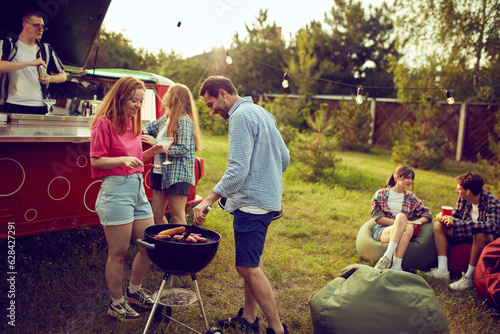 Group of young people, friends spending time outdoors, having barbecue party, cooking, drinking cocktails, talking. Countryside meeting. Concept of friendship, leisure time, weekends, summer, party