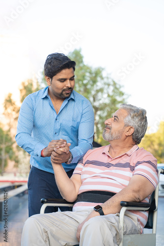 Young man giving support to sick old man in a wheel chair.