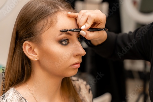 Make-up artist paints eyebrow pencil to beautiful brunette in be