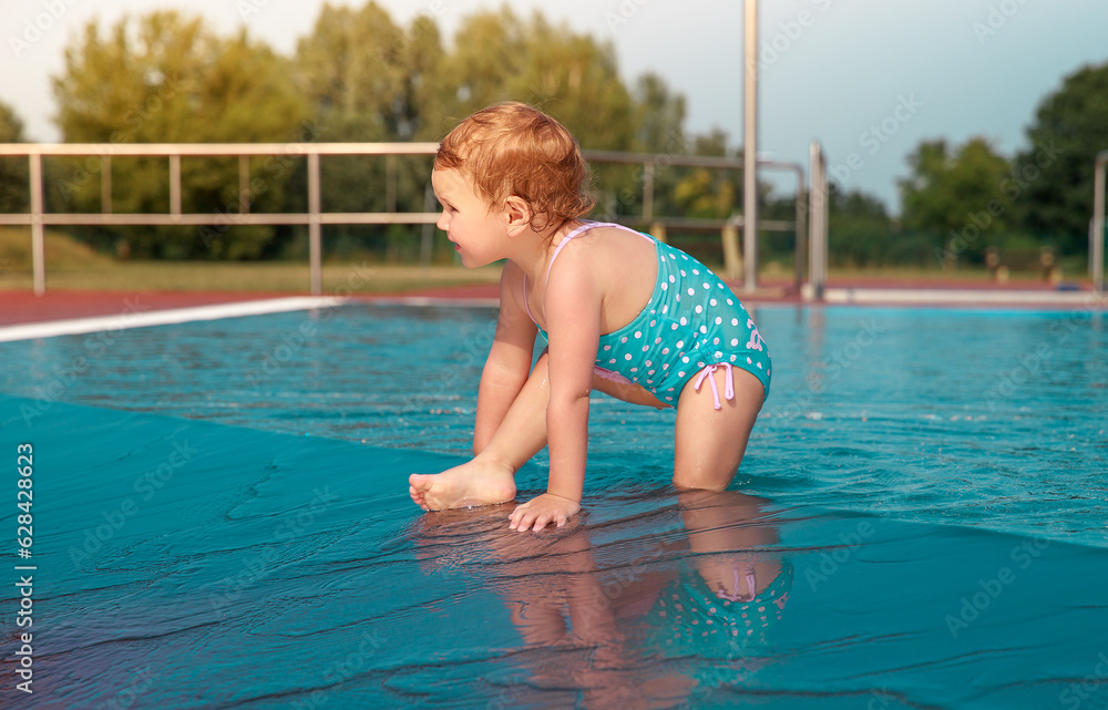 Little girl is playing in the pool. Happy child outside in the water. Pretty girl in a blue bathing suit.
