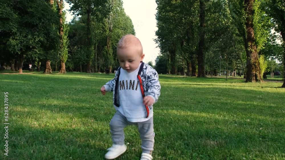 Baby takes first steps. Baby boy running in the park. Happy baby takes first steps in nature. Toddler walks on grass in park. Baby learns to walk. Happy family kid concept 4k