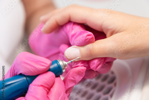 A manicurist in pink medical gloves files the cuticle of the client with a hardware file. Close-up, top view. Concept of salon professional manicure