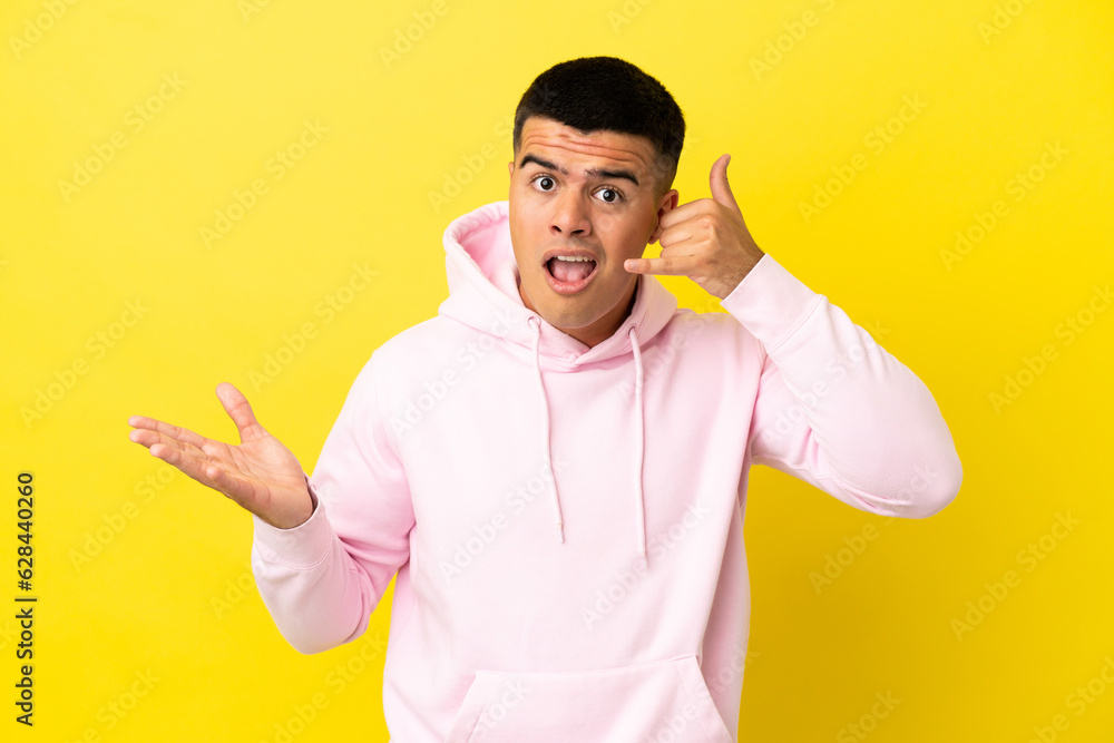 Young handsome man over isolated yellow background making phone gesture and doubting Young handsome man over isolated yellow background making phone gesture and doubting