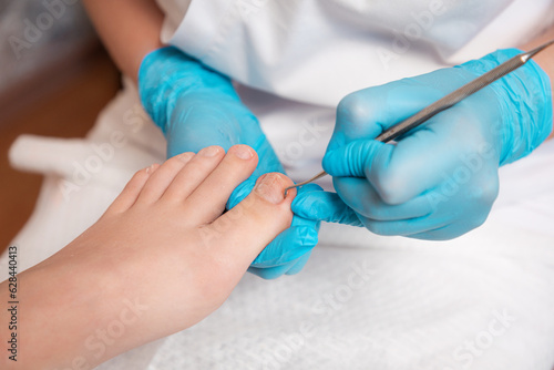 Chiropodist does a pedicure for the client's foot, cleaning the nails with a double-sided curette. Close up. The concept of salon professional nail care and podology