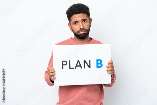 Young Brazilian man isolated on white background holding a placard with the message PLAN B with sad expression