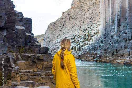 Hiker woman in yellow jacket visiting Studlagil Canyon, Iceland. Famous touristic landmark destination with volcanic basalt columns. photo