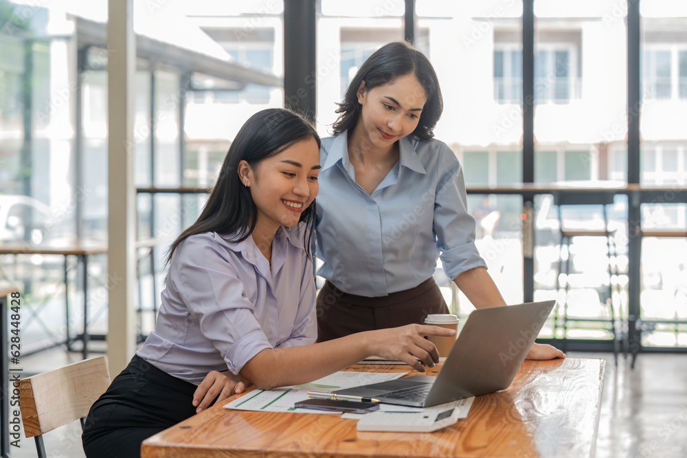 Two young Asian businesswoman discuss investment project working and planning strategy. Business people talking together with laptop computer at office Two young Asian businesswoman discuss investment project working and planning strategy. Business people talking together with laptop computer at office