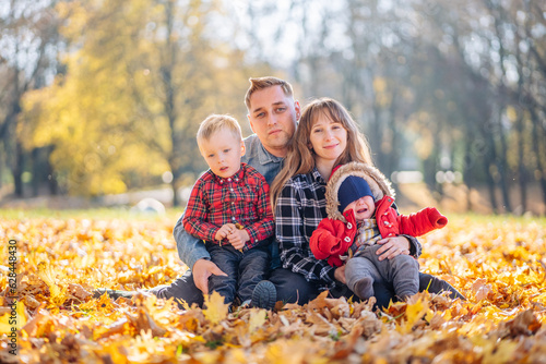 A young family sits in the park on a leafy, sunny autumn day.