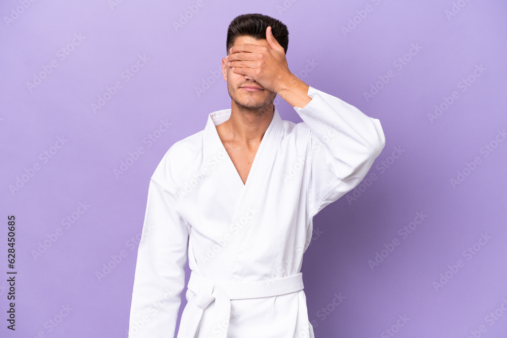 Young caucasian man doing karate isolated on purple background covering eyes by hands. Do not want to see something Young caucasian man doing karate isolated on purple background covering eyes by hands. Do not want to see something