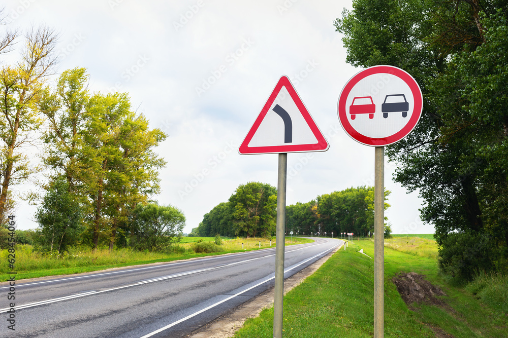 Road signs, overtaking is prohibited and a dangerous turn on the background of the track Road signs, overtaking is prohibited and a dangerous turn on the background of the track