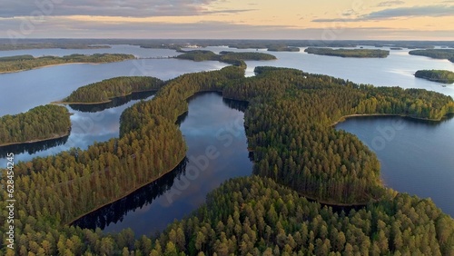 Flying over lakeland in Finland. Aerial shot of many green islands at sunset - classical Finnish landscape. Finnish Lake land in sunset lights. Green islands and lake with clouds reflection. 4K, UHD