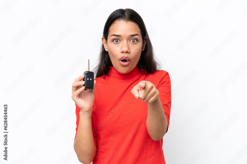 Young Colombian woman holding car keys isolated on white background surprised and pointing front Young Colombian woman holding car keys isolated on white background surprised and pointing front