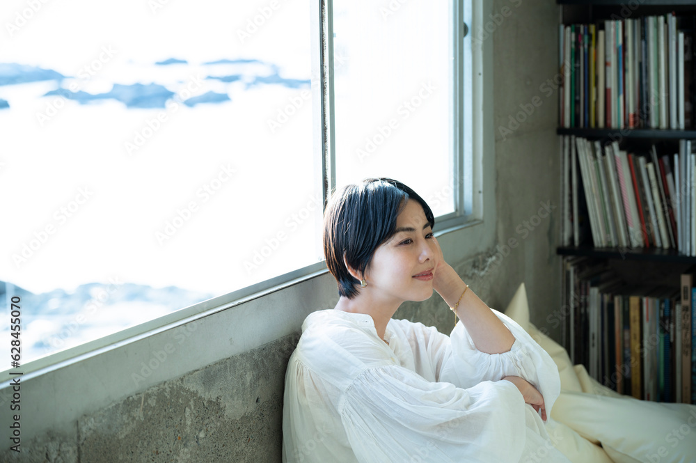 Asian woman with short cut hair sitting relaxed in a room with bookshelves Asian woman with short cut hair sitting relaxed in a room with bookshelves