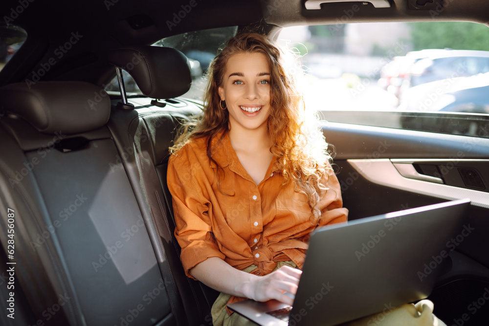 Business beautiful woman with a modern laptop sits in the back seat of a car. Successful startup, remote work. Freelance. 