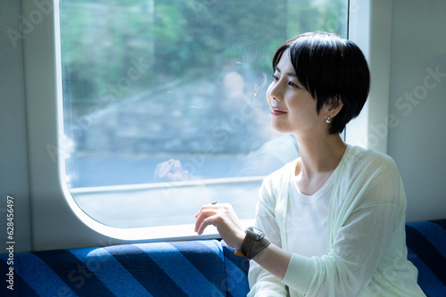 A Japanese woman is sitting on a train seat and enjoying the scenery outside the window. Travelling on public transportation