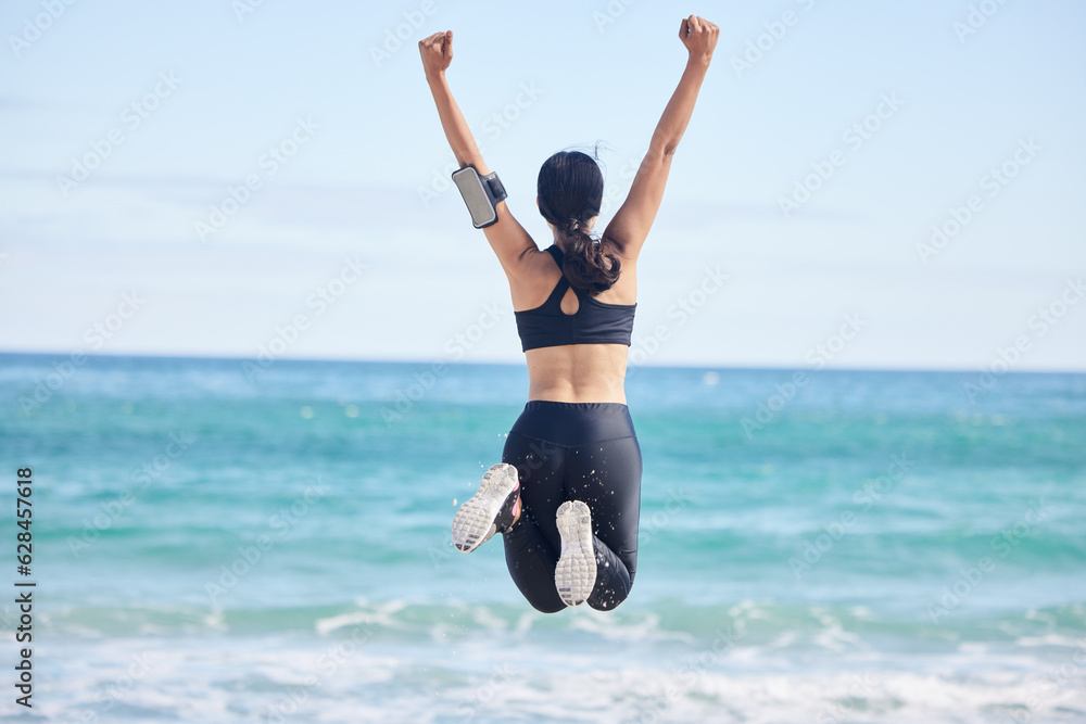 Happy woman, fitness and jump in achievement on beach for winning, workout success or outdoor exercise. Rear view of excited female person in celebration for accomplishment or training by the ocean Happy woman, fitness and jump in achievement on beach for winning, workout success or outdoor exercise. Rear view of excited female person in celebration for accomplishment or training by the ocean