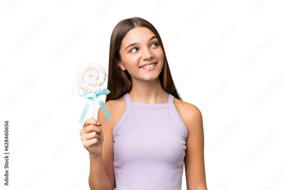 Teenager caucasian girl holding a lollipop over isolated background looking up while smiling Teenager caucasian girl holding a lollipop over isolated background looking up while smiling