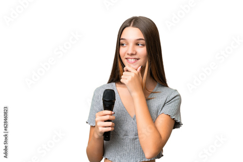 Teenager singer girl picking up a microphone over isolated background looking to the side and smiling